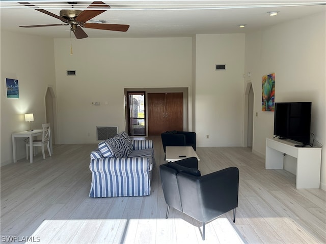 living room featuring light hardwood / wood-style flooring, ceiling fan, and a towering ceiling