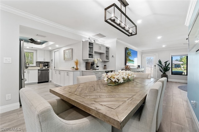 dining room with a tray ceiling, crown molding, a wealth of natural light, and light hardwood / wood-style floors