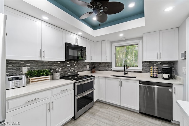 kitchen with sink, white cabinetry, stainless steel appliances, tasteful backsplash, and a tray ceiling