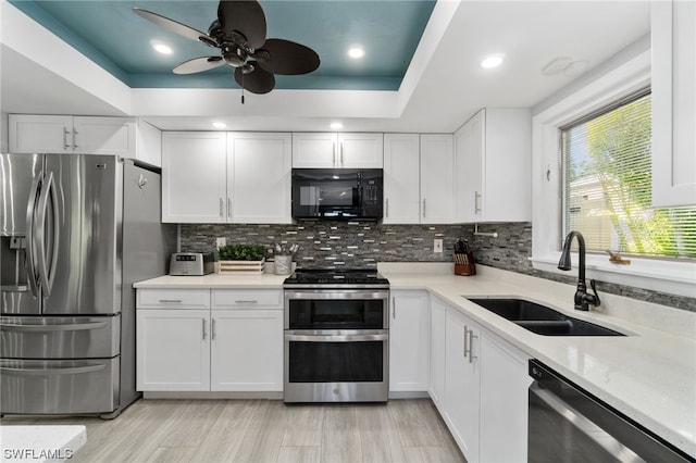 kitchen featuring stainless steel appliances, sink, white cabinets, and a tray ceiling