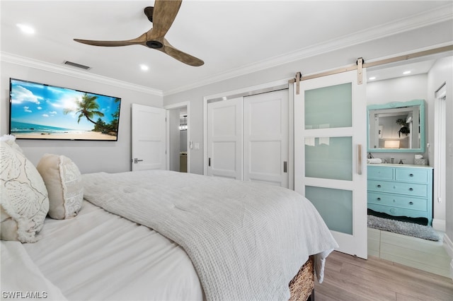 bedroom featuring ornamental molding, ceiling fan, light hardwood / wood-style floors, a barn door, and a closet