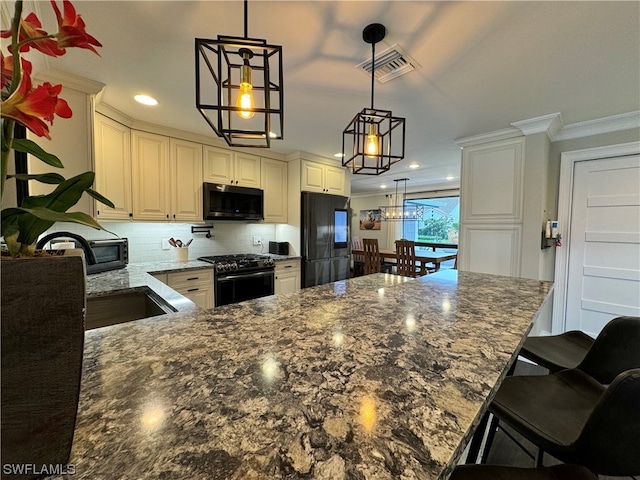 kitchen with dark stone counters, black appliances, hanging light fixtures, backsplash, and ornamental molding