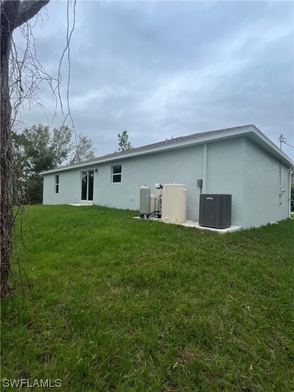 rear view of property featuring cooling unit and a lawn