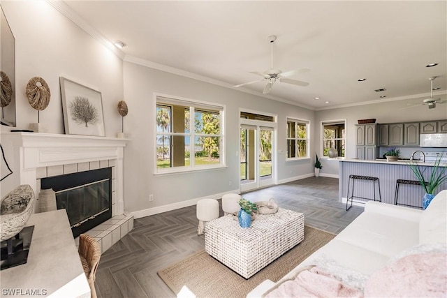 living area featuring a fireplace, visible vents, a ceiling fan, baseboards, and ornamental molding