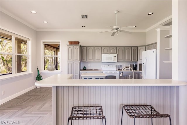 kitchen featuring a breakfast bar, crown molding, light countertops, gray cabinetry, and white appliances