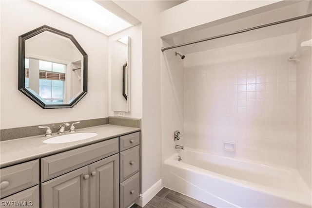 bathroom with bathtub / shower combination, vanity, baseboards, and wood finished floors