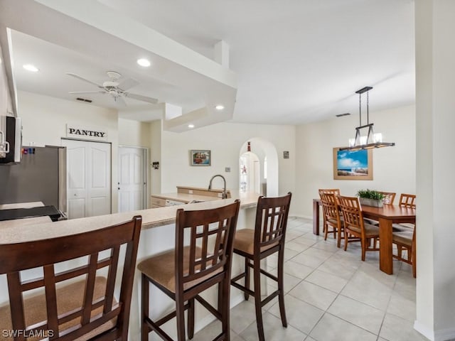 kitchen with light tile patterned flooring, a breakfast bar, stainless steel fridge, pendant lighting, and ceiling fan