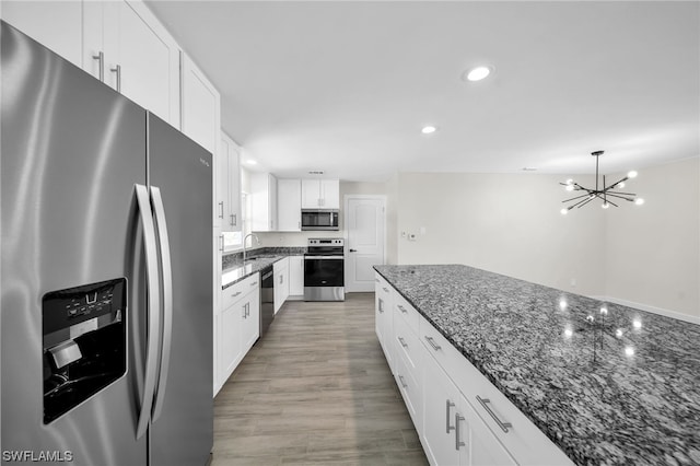 kitchen with an inviting chandelier, stainless steel appliances, dark stone countertops, white cabinets, and hardwood / wood-style flooring