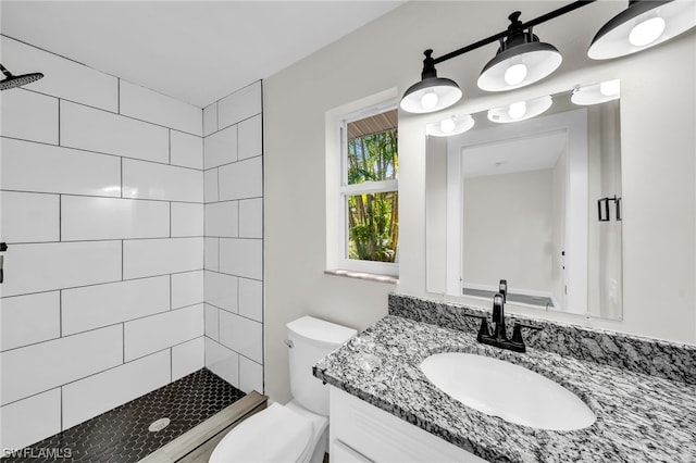 bathroom featuring vanity, a tile shower, and toilet