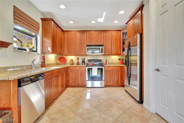 kitchen with light stone countertops, light tile patterned floors, stainless steel appliances, and sink