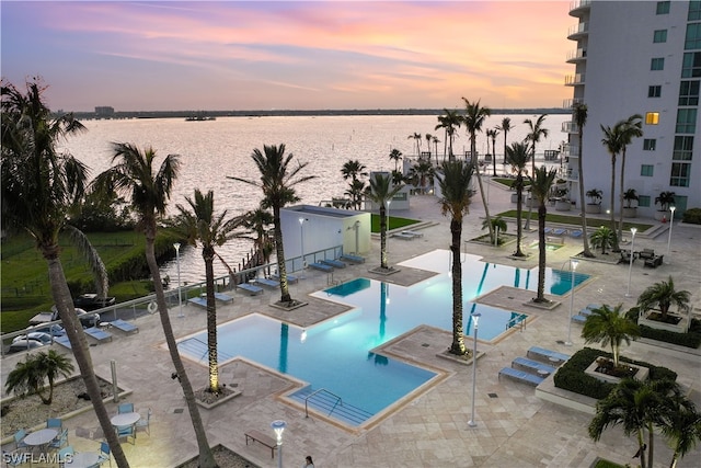 pool at dusk featuring a water view and a patio area