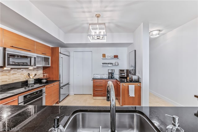 kitchen with appliances with stainless steel finishes, decorative light fixtures, tasteful backsplash, sink, and dark stone countertops