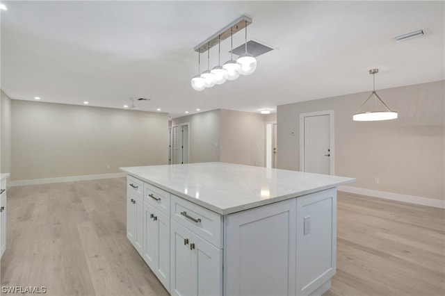 kitchen featuring hanging light fixtures, white cabinets, a center island, light stone counters, and light hardwood / wood-style floors