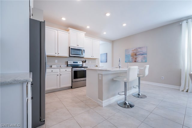 kitchen featuring white cabinetry, a breakfast bar, light tile patterned floors, appliances with stainless steel finishes, and a center island with sink