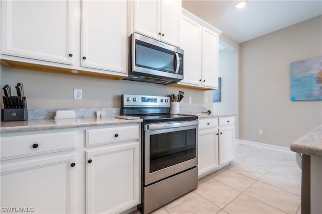 kitchen with appliances with stainless steel finishes, light tile patterned floors, white cabinets, and light stone countertops