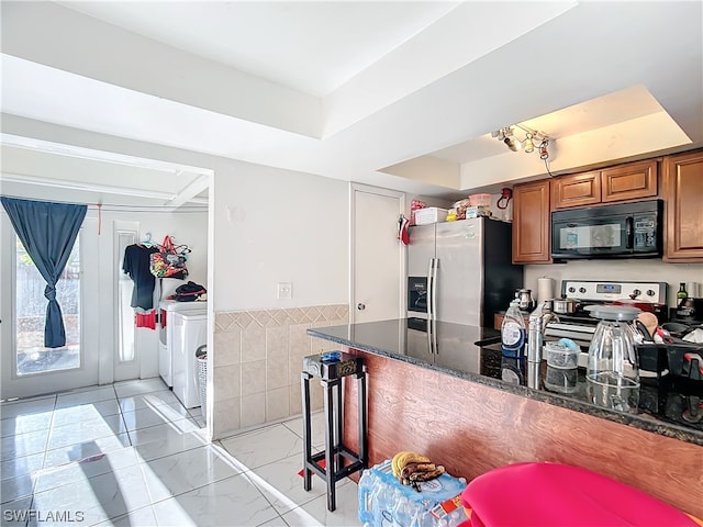 kitchen with kitchen peninsula, dark stone counters, stainless steel appliances, tile walls, and washer and dryer