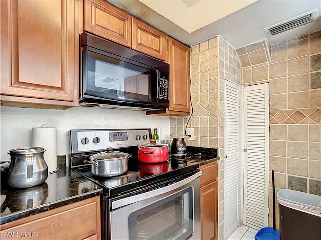 kitchen featuring decorative backsplash, tile walls, dark stone countertops, and electric range