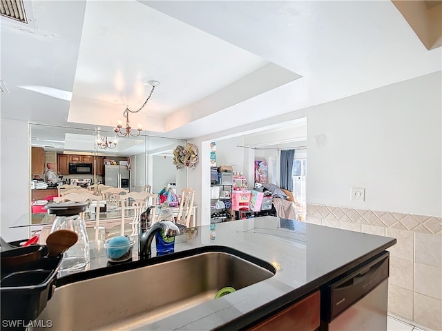 kitchen featuring pendant lighting, a tray ceiling, sink, a notable chandelier, and stainless steel appliances