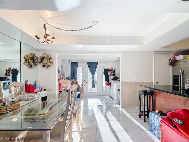 dining space featuring tile walls, washing machine and clothes dryer, french doors, and a chandelier