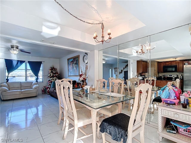 dining space with ceiling fan with notable chandelier and a raised ceiling