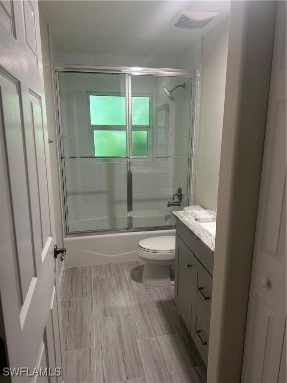 full bathroom with enclosed tub / shower combo, vanity, and toilet