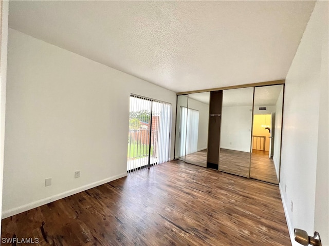 unfurnished bedroom with a textured ceiling, access to outside, a closet, and hardwood / wood-style flooring