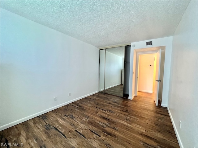 unfurnished bedroom with a textured ceiling, dark wood-type flooring, and a closet