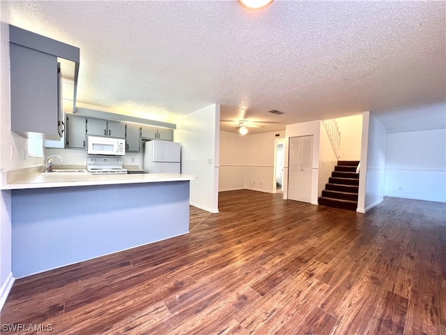 kitchen with white appliances, kitchen peninsula, dark wood-type flooring, and a textured ceiling