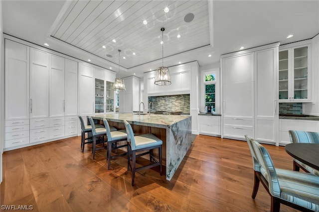 kitchen featuring decorative backsplash, an island with sink, hardwood / wood-style floors, white cabinets, and a raised ceiling