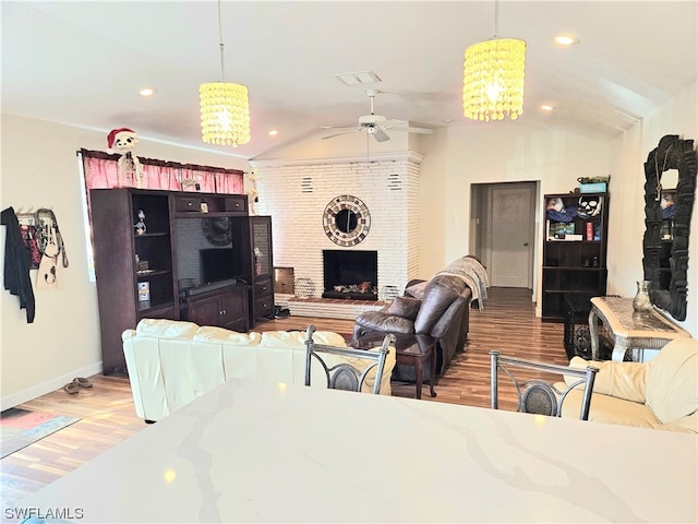 living room with lofted ceiling, ceiling fan with notable chandelier, hardwood / wood-style flooring, and a brick fireplace