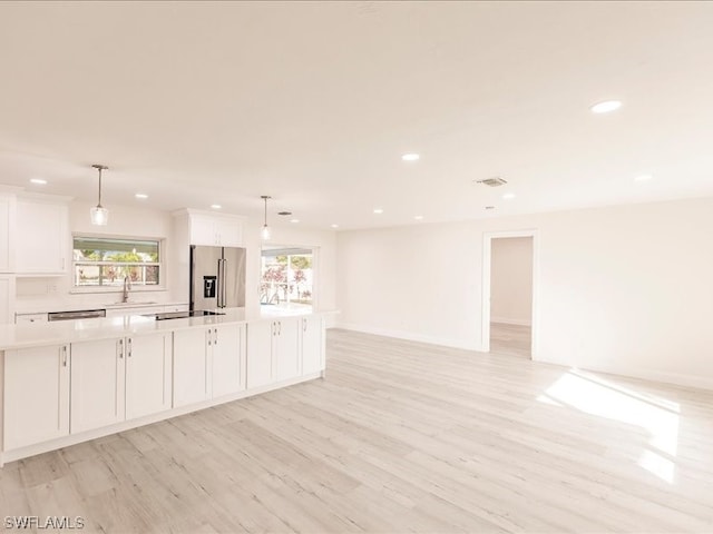 interior space featuring pendant lighting, a kitchen island, white cabinets, stainless steel fridge, and light wood-type flooring