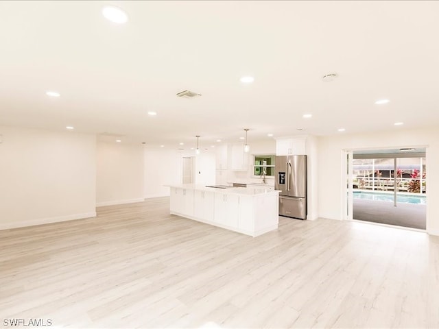 kitchen featuring hanging light fixtures, stainless steel fridge, light wood-type flooring, white cabinets, and a center island