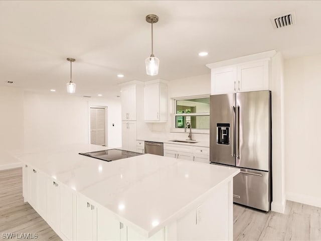 kitchen with appliances with stainless steel finishes, white cabinetry, light hardwood / wood-style floors, and pendant lighting