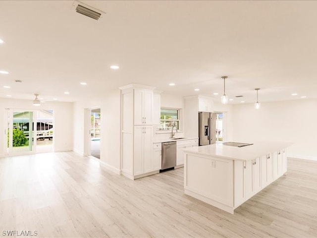 kitchen with decorative light fixtures, appliances with stainless steel finishes, light wood-type flooring, white cabinets, and a center island