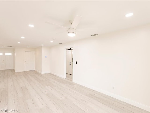 spare room with a barn door, light hardwood / wood-style floors, and ceiling fan