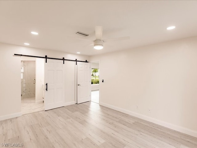 spare room with a barn door, ceiling fan, and light hardwood / wood-style flooring