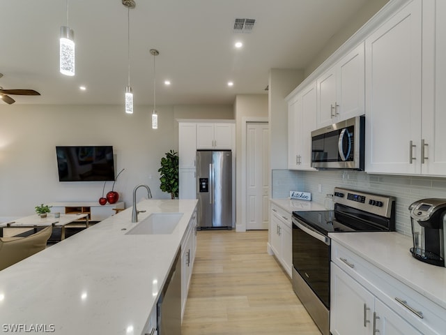 kitchen with pendant lighting, ceiling fan, sink, white cabinets, and stainless steel appliances