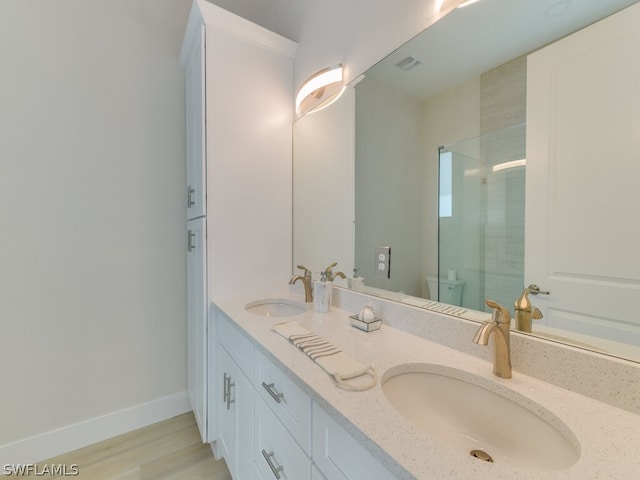 bathroom featuring toilet, wood-type flooring, and dual bowl vanity