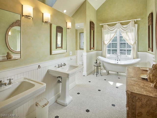 bathroom with dual sinks, lofted ceiling, a tub to relax in, tile patterned floors, and toilet