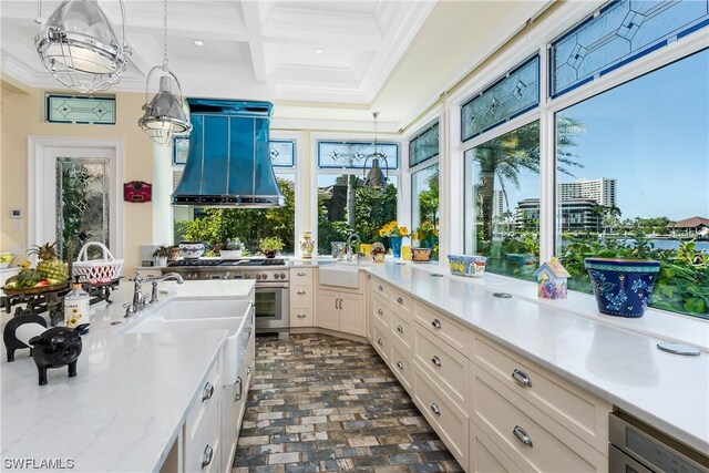 kitchen with custom exhaust hood, coffered ceiling, sink, and decorative light fixtures