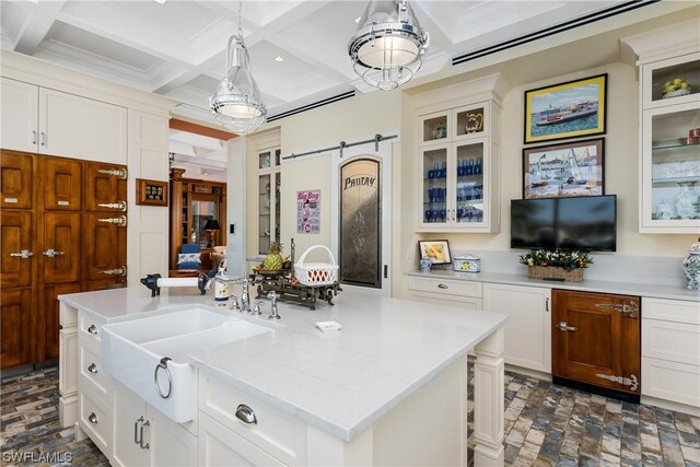 kitchen featuring coffered ceiling, pendant lighting, white cabinets, a center island with sink, and beam ceiling