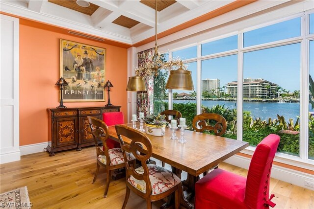 dining space with beam ceiling, a water view, ornamental molding, coffered ceiling, and light wood-type flooring