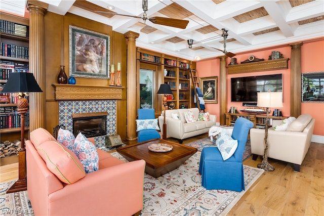 living room with coffered ceiling, light wood-type flooring, built in features, ceiling fan, and a tile fireplace