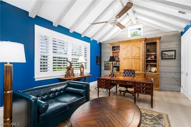 home office with ceiling fan, wooden walls, light hardwood / wood-style floors, and vaulted ceiling with beams