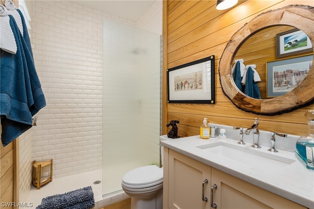 bathroom with tiled shower, vanity, wood walls, and toilet