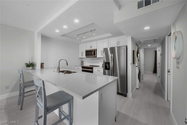 kitchen with track lighting, stainless steel appliances, white cabinets, sink, and kitchen peninsula