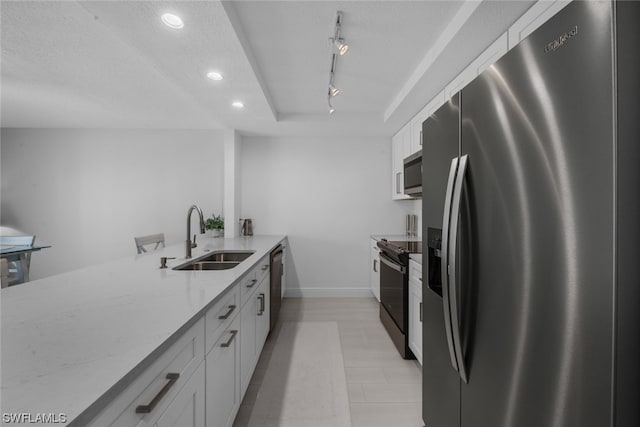 kitchen with kitchen peninsula, white cabinets, light stone counters, stainless steel appliances, and sink