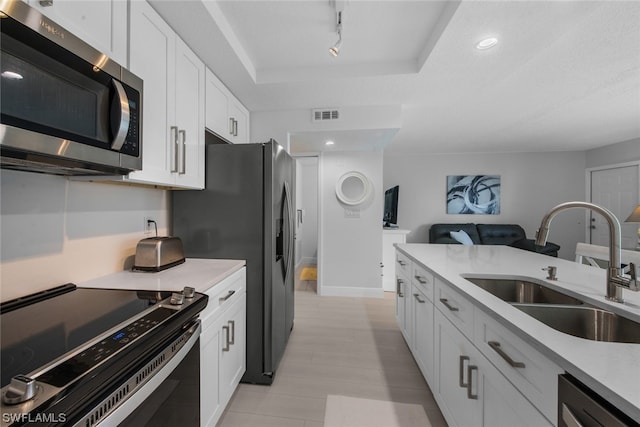 kitchen with sink, appliances with stainless steel finishes, white cabinetry, and a raised ceiling