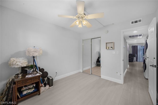 bedroom with washer / dryer, ceiling fan, light wood-type flooring, and a closet