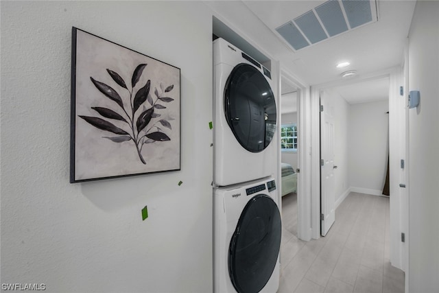 clothes washing area featuring stacked washing maching and dryer and light hardwood / wood-style flooring